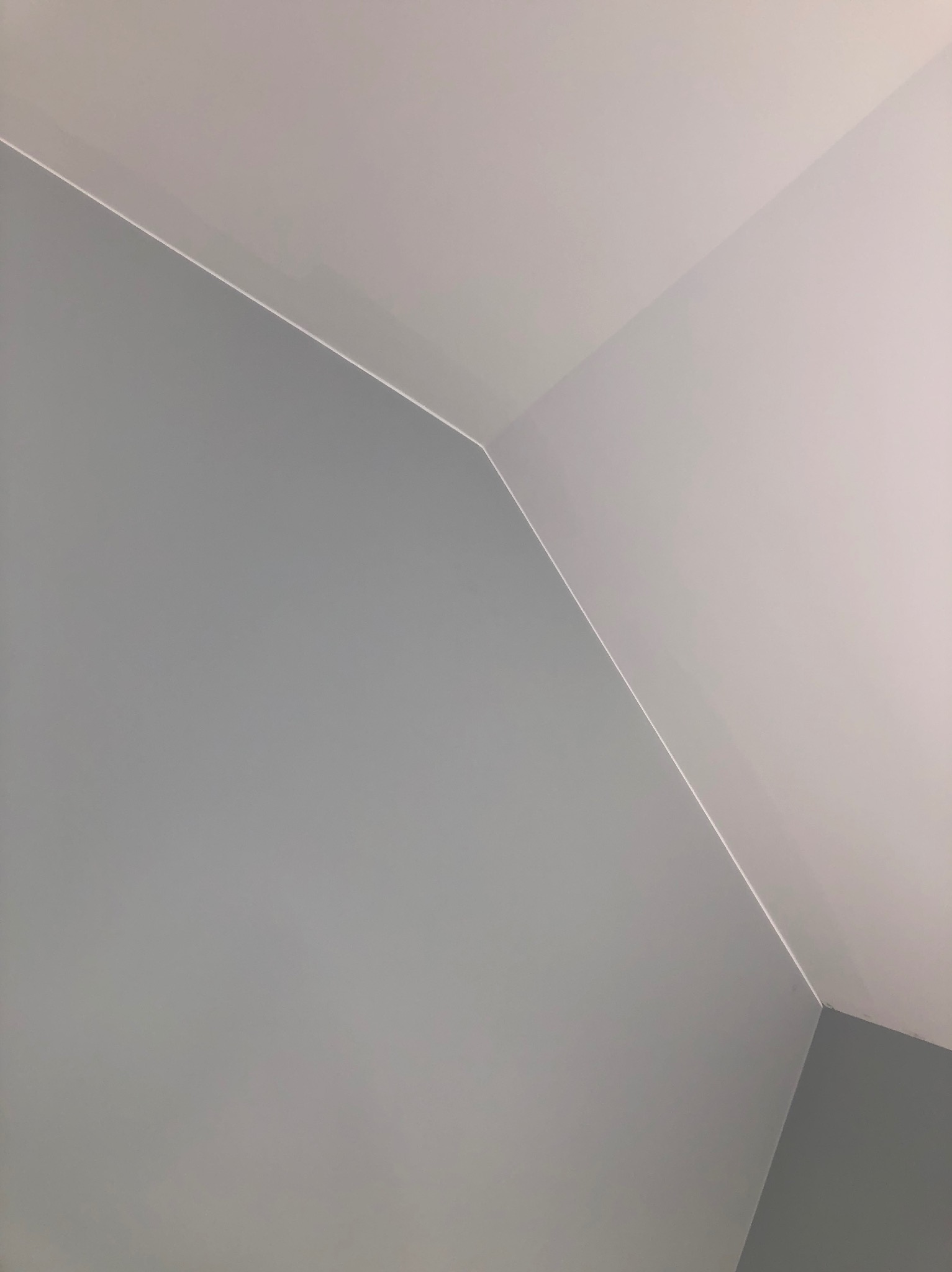 Ściana i sufit po malowaniu na szaro i biało, widoczne ostre krawędzie i kąty, minimalistyczne ujęcie z dołu.