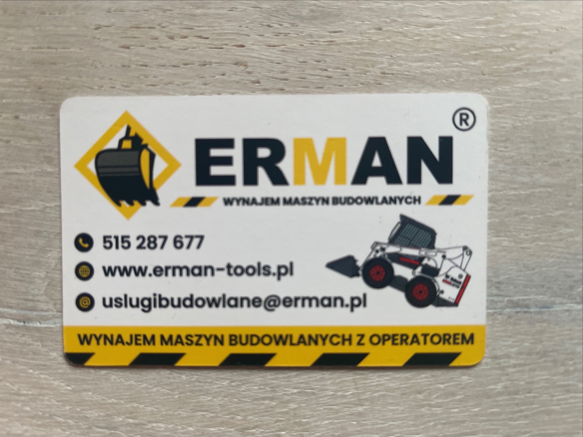 Wizytówka firmy ERMAN oferującej wynajem maszyn budowlanych, z ikoną koparki i minikoparki, numerem telefonu, adresem strony internetowej i adresem e-mail.