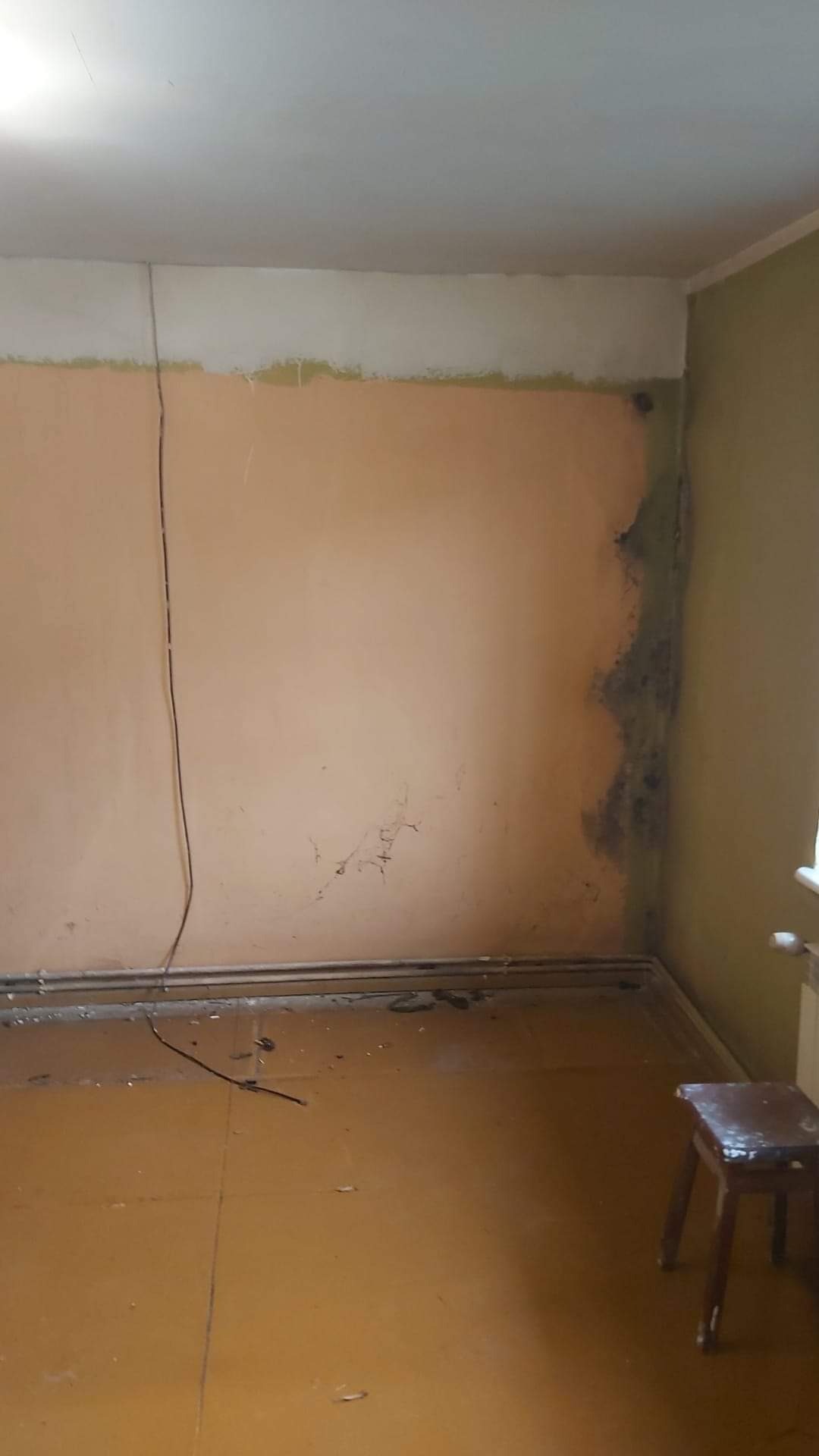 Pokój przed remontem: widoczne plamy wilgoci na ścianie, stara farba i przygotowany fragment ściany pod sufit do dalszych prac wykończeniowych.