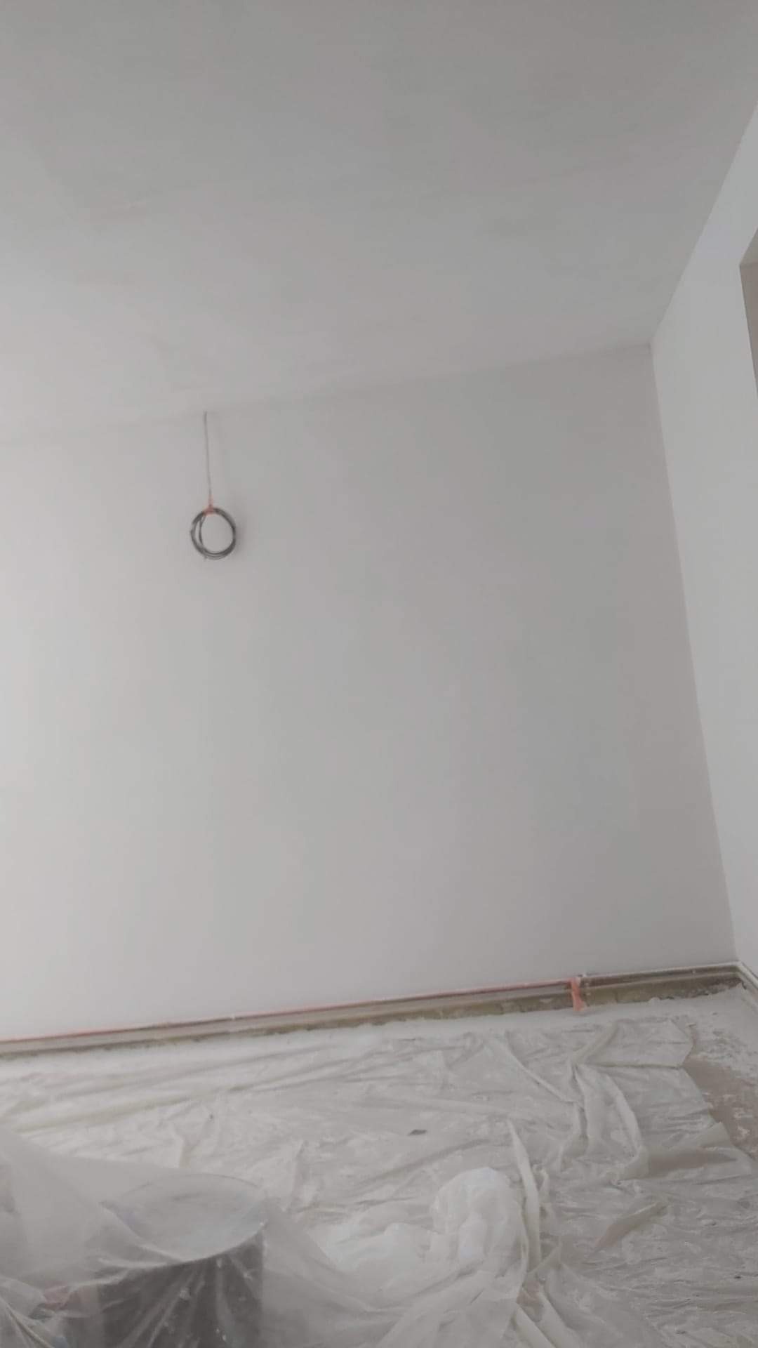 Świeżo pomalowane na biało wnętrze pokoju z zabezpieczoną folią podłogą i wystającymi kablami ze ściany.