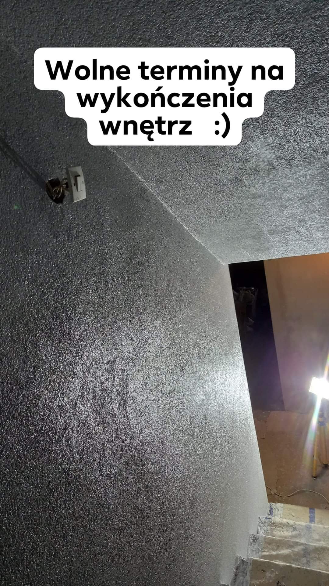 Ściana i sufit pokryte szarą, ziarnistą strukturą, widoczne schody w tle, z informacją tekstową o wolnych terminach na prace wykończeniowe.
