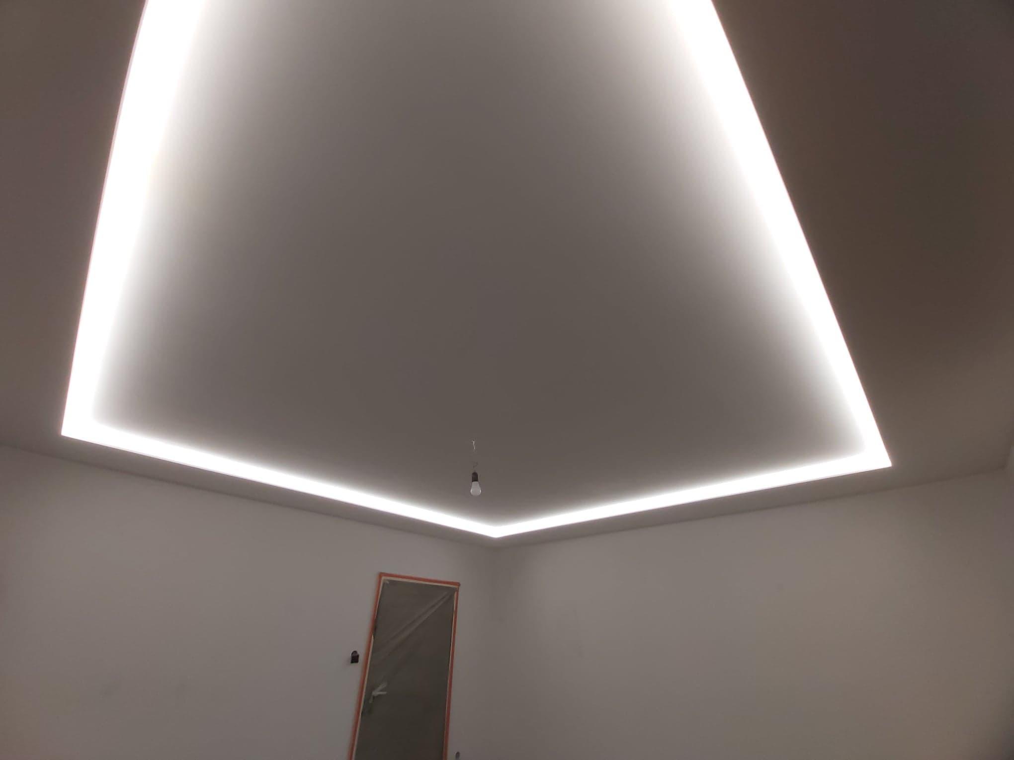 Nowoczesne oświetlenie sufitowe LED w kształcie prostokąta, podwieszany sufit w jasnym pomieszczeniu z widocznym wejściem.