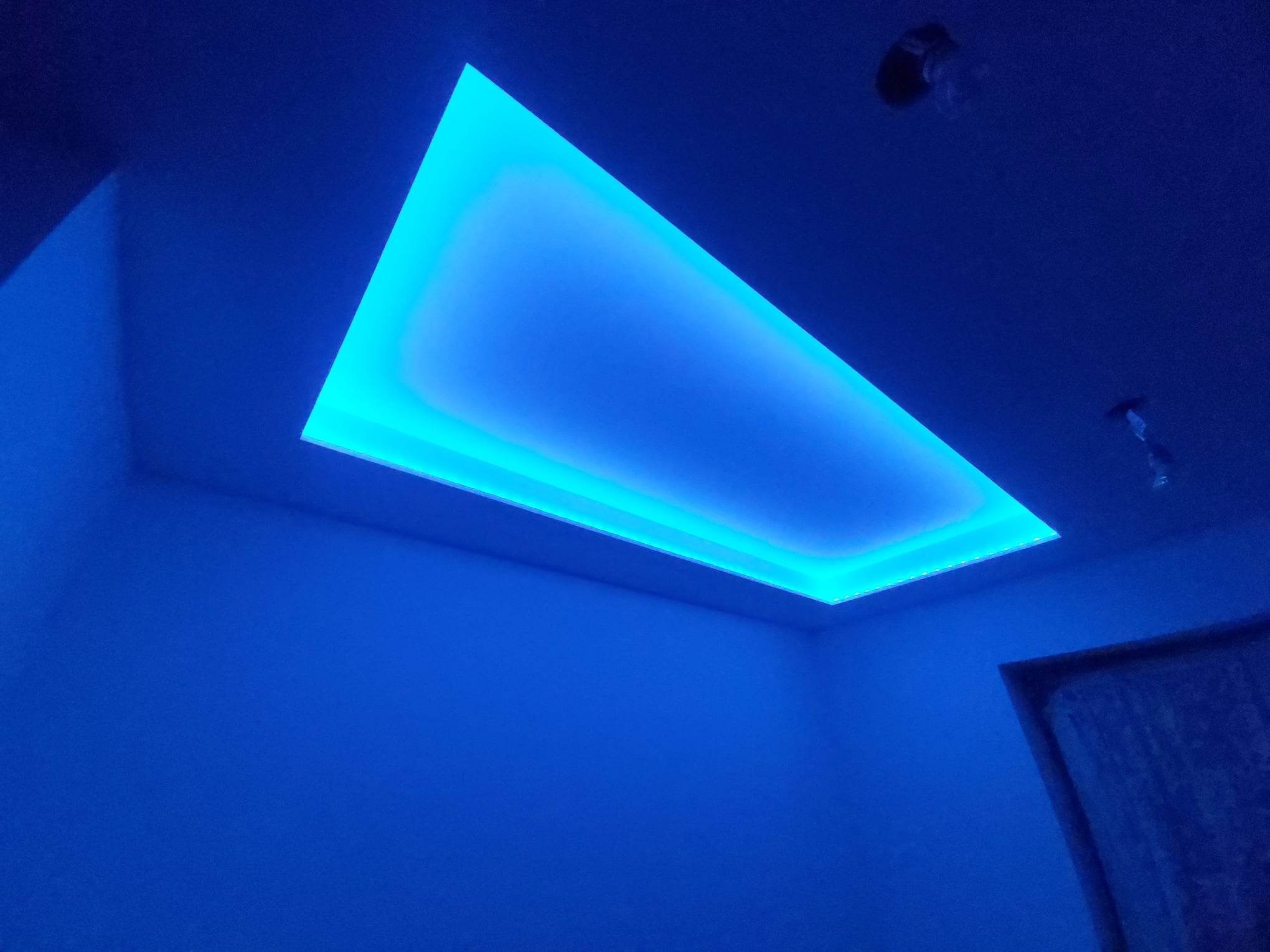 Nowoczesne oświetlenie sufitowe LED w kształcie prostokąta, emitujące intensywne niebieskie światło, w pomieszczeniu o ścianach pomalowanych na podobny odcień niebieskiego.