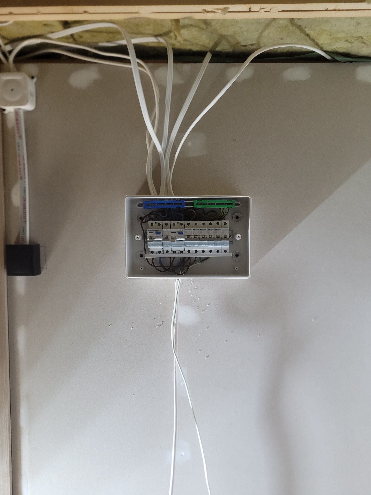 Szara skrzynka rozdzielcza z zamontowanymi bezpiecznikami i podłączonymi przewodami elektrycznymi, umieszczona na ścianie w trakcie montażu instalacji elektrycznej.