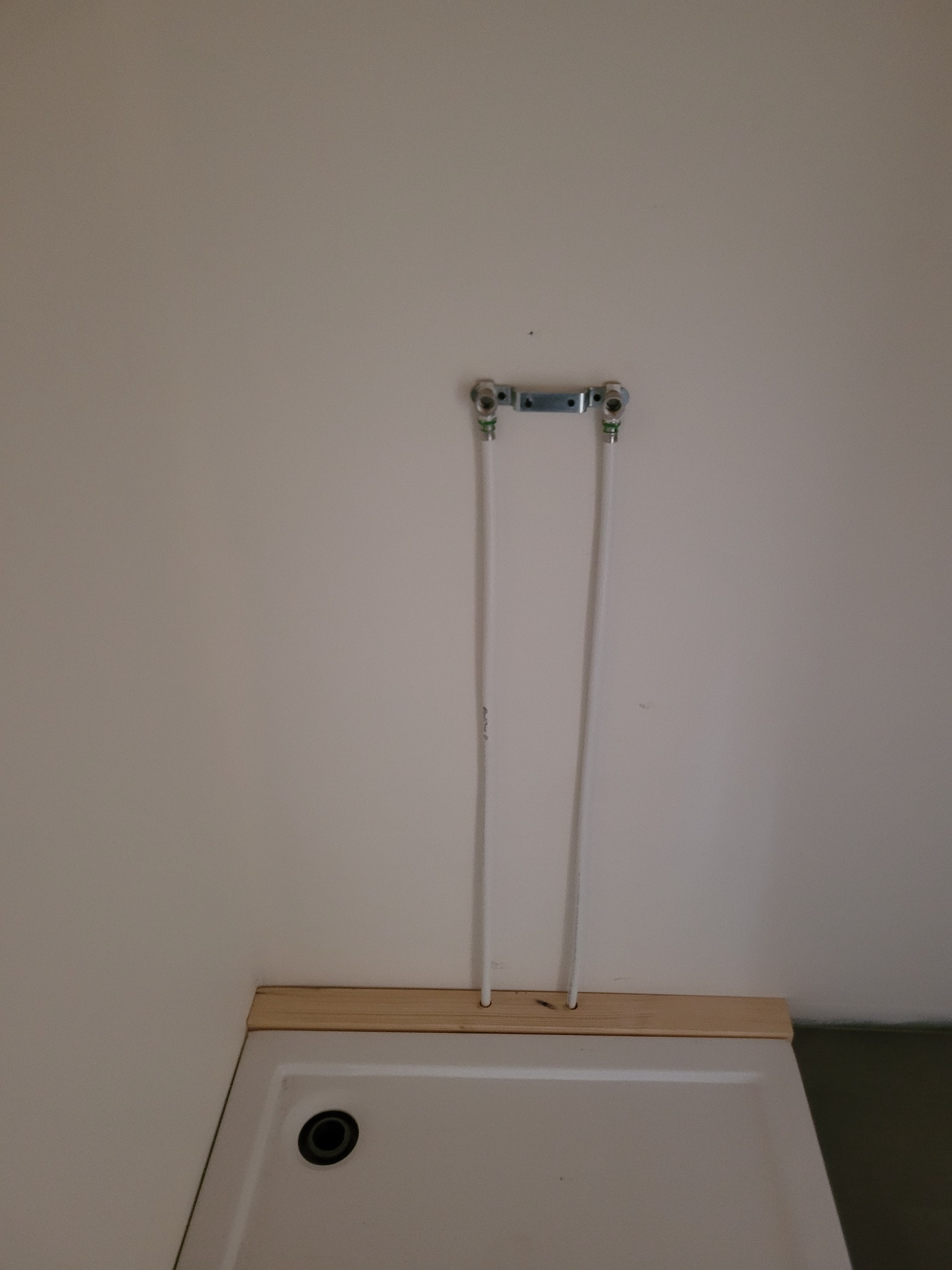 Przyłącze wodne do brodzika z rurami pex mocowanymi do ściany za pomocą metalowej listwy. Widoczne otwory w drewnianej listwie pod brodzikiem.