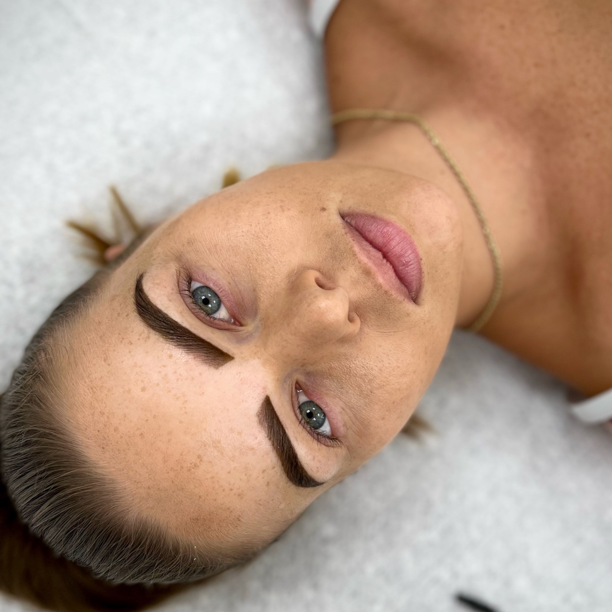 Kobieta z brązowymi brwiami po zabiegu makijażu permanentnego, widoczne piegi i delikatny makijaż ust.