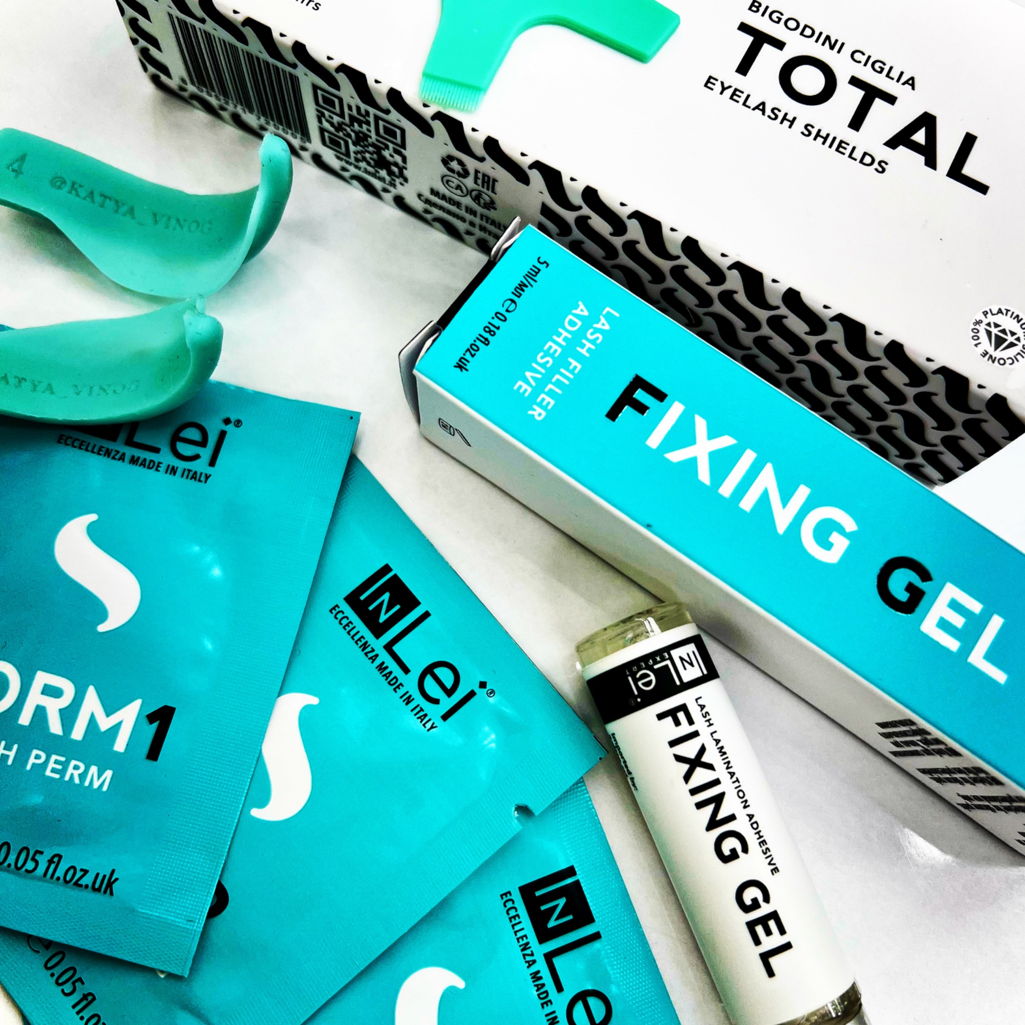 Zestaw do liftingu rzęs: silikonowe podkładki, klej, utrwalacz i preparat do trwałej ondulacji, marki InLei i Bigodini Ciglia Total, na białym tle.