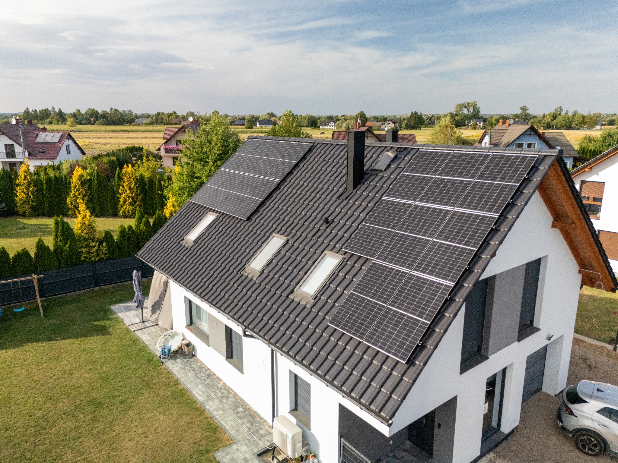 Fotowoltaika na dachu domu jednorodzinnego w Niepołomicach. Widok z góry ukazuje panele słoneczne, okna dachowe i zadbany ogród. Nowoczesna instalacja.