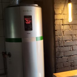 Gekon ENERGIA - Biały bojler Haier Eco Life z wyświetlaczem pokazującym temperaturę 41 stopni Celsjusza, zamontowany w pomieszczeniu z ceglaną ścianą i wiszącą żarówką.