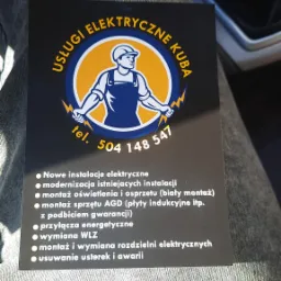 Wizytówka firmy 'Usługi Elektryczne Kuba' leżąca na spodniach, z logo przedstawiającym elektryka trzymającego błyskawice oraz listą oferowanych usług.