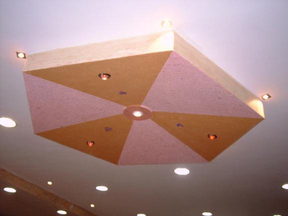Dekoracyjny sufit podwieszany z geometrycznym wzorem w odcieniach różu i beżu, oświetlony punktowymi lampami halogenowymi.