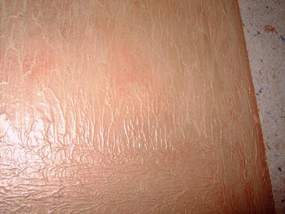 Tekstura ściany pokryta stiukiem w odcieniach brzoskwini i bieli, z widocznymi smugami i nierównościami.