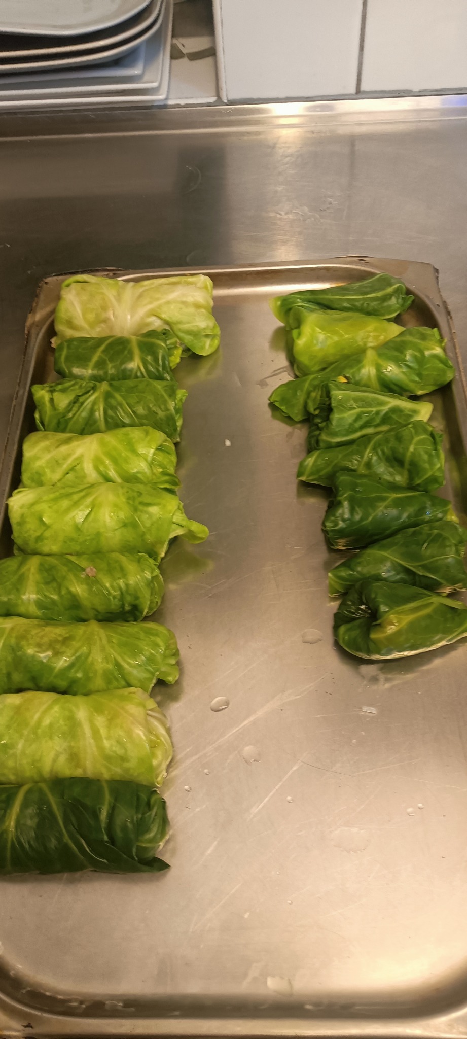 Rządki świeżo przygotowanych gołąbków z kapusty na metalowej tacy w kuchni restauracyjnej.