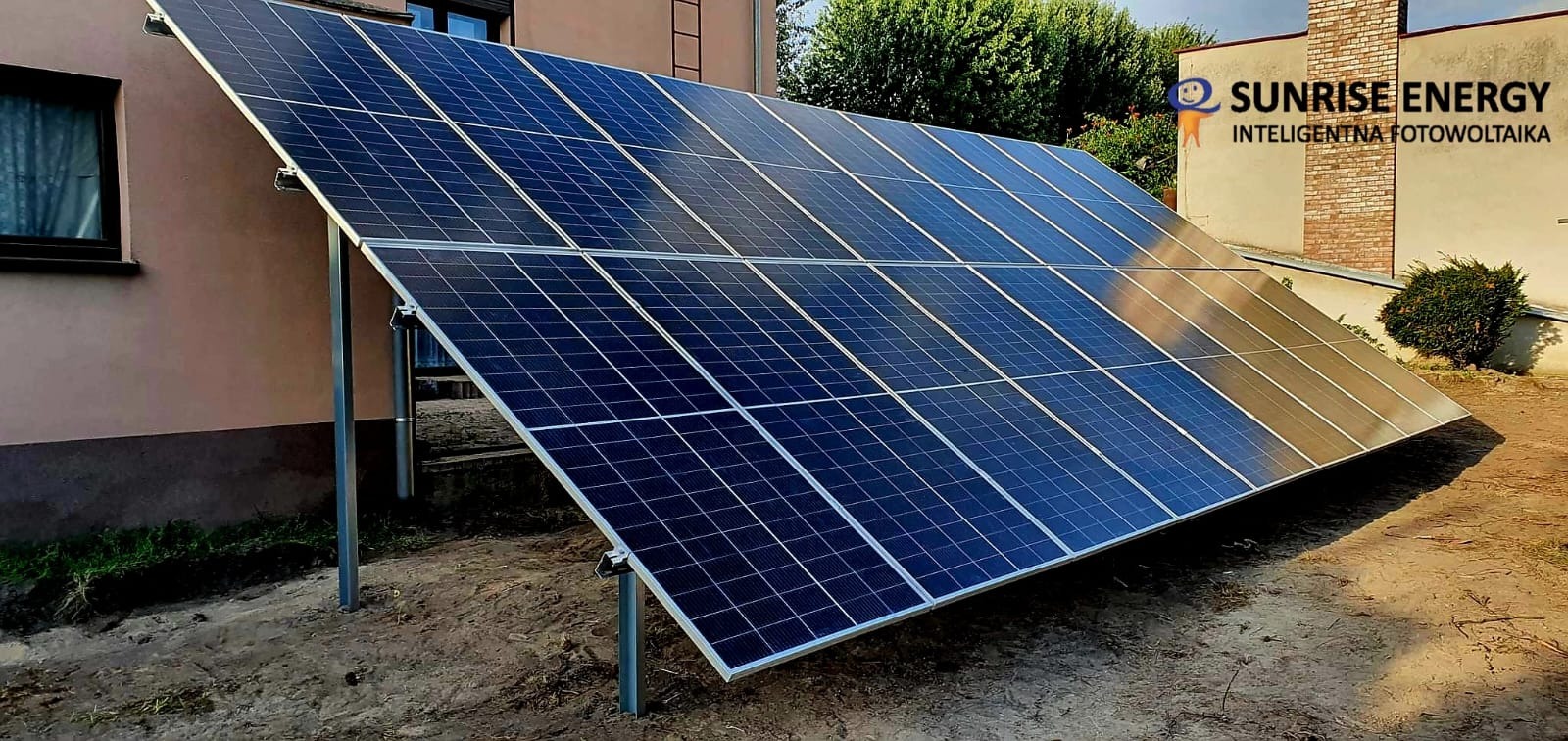 Instalacja fotowoltaiczna na gruncie, widoczne panele słoneczne na metalowej konstrukcji, logo firmy Sunrise Energy w prawym górnym rogu.