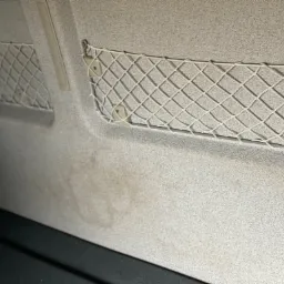 Wnętrze samochodu z widocznymi zabrudzeniami na tapicerce i siatkami na drobiazgi po bokach.