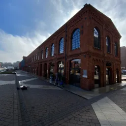 Długi, ceglany budynek z łukowymi oknami po umyciu elewacji, z widocznymi śladami mokrej nawierzchni i sprzętem do mycia ciśnieniowego w tle.