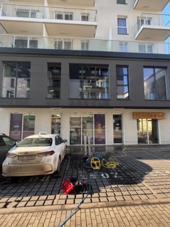 Elewacja budynku usługowego z widocznymi śladami po myciu, na chodniku rozłożony sprzęt do czyszczenia, obok zaparkowany samochód z taksówką na dachu.