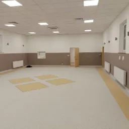 Przestronne, nowo wykończone wnętrze z jasną podłogą z wzorem, białymi ścianami i brązową lamperią, grzejnikami oraz drewnianymi drzwiami w tle.