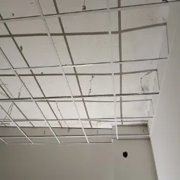 Metalowa konstrukcja sufitu podwieszanego, widoczna instalacja elektryczna, surowy stan, przygotowanie do montażu płyt.