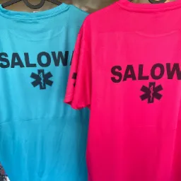 Dwie koszulki sportowe, turkusowa i różowa, z czarnym nadrukiem 'SALOW' i symbolem medycznym, wiszące na wieszakach na tle regału sklepowego.