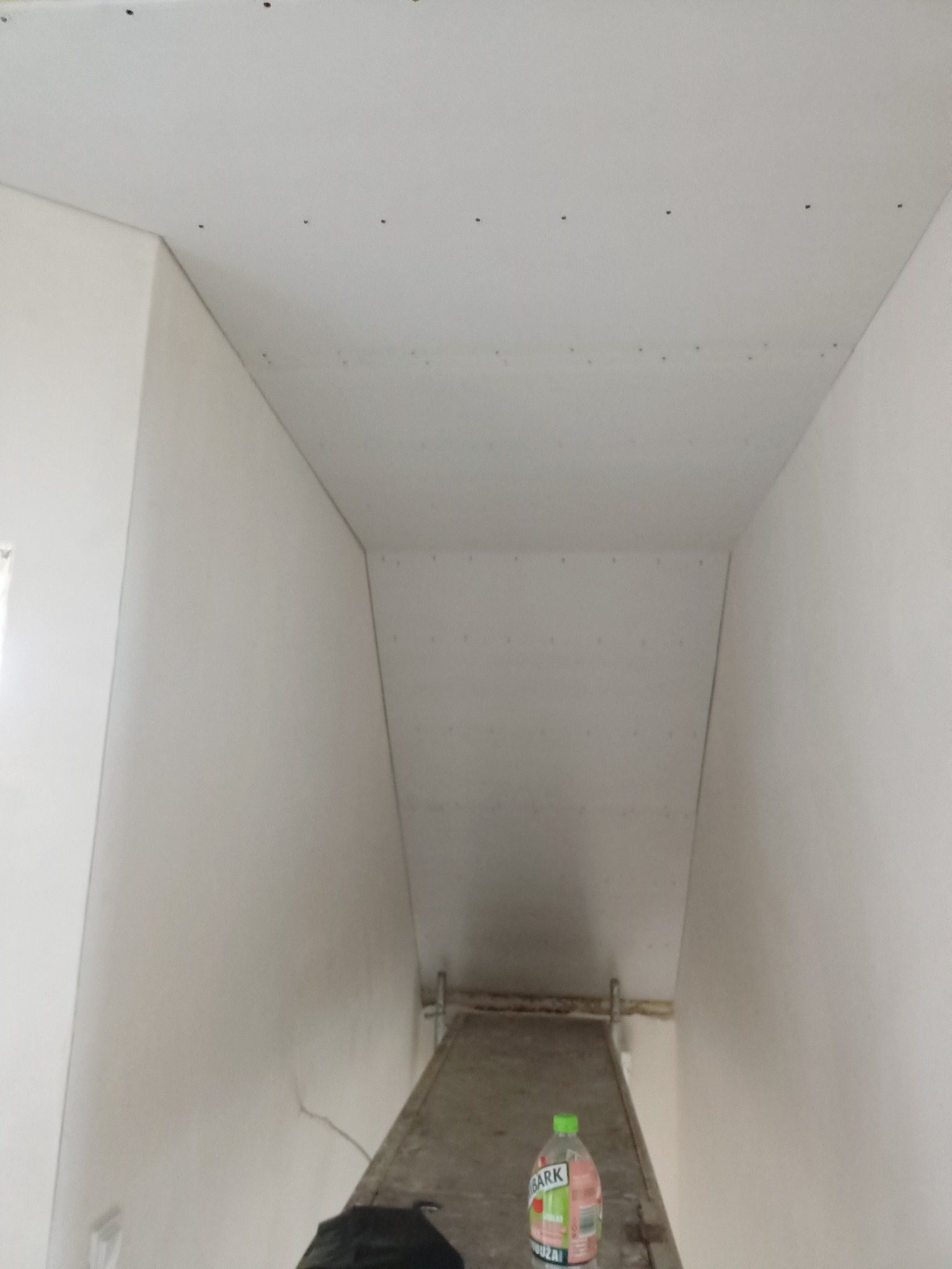 Sufit i ściany wykończone płytami karton gips w Szczecinie, widoczne ślady po wkrętach, butelka wody na rusztowaniu w tle.