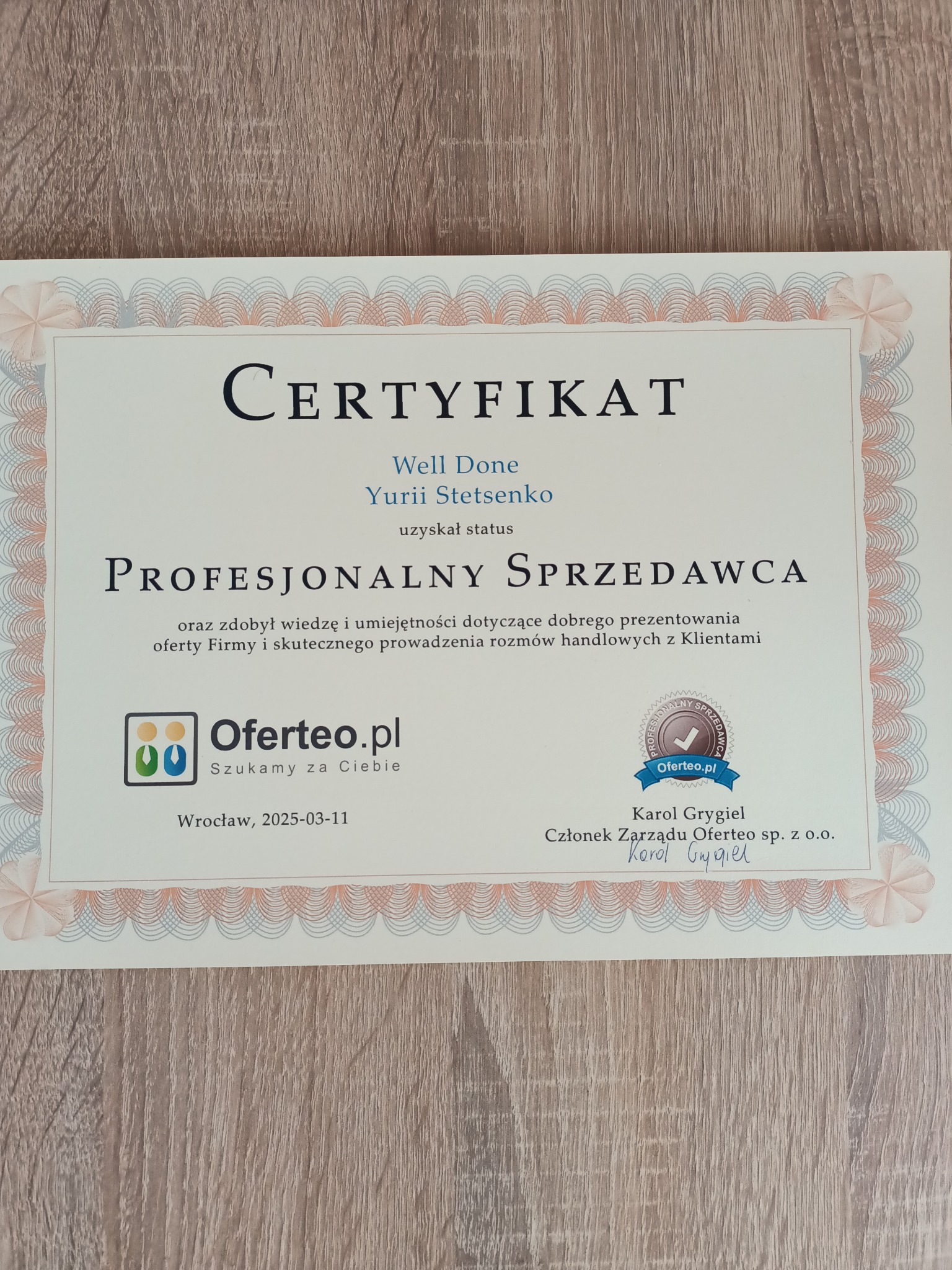 Certyfikat Oferteo dla Yurii Stetsenko, potwierdzający status Profesjonalnego Sprzedawcy, leżący na drewnianej powierzchni. Dokument datowany na 11 marca 2025 r.