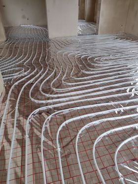 Białe rurki ogrzewania podłogowego ułożone na folii z siatką w pomieszczeniu w trakcie montażu, widok z góry, Mława.
