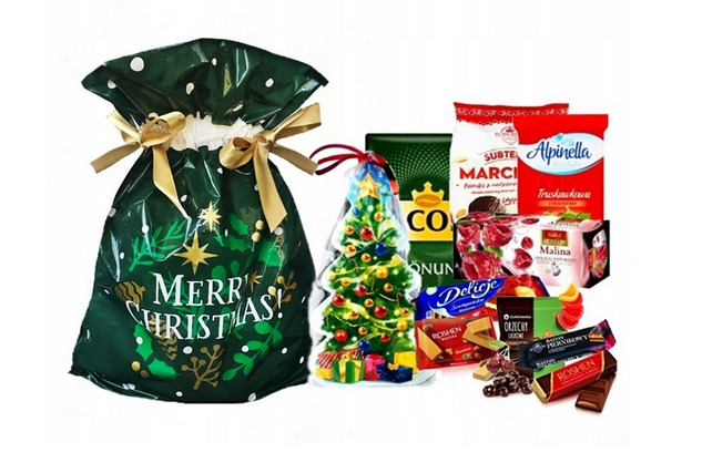 Świąteczny zestaw upominkowy z zieloną torbą z napisem 'Merry Christmas', czekoladowym drzewkiem w przezroczystym opakowaniu, kawą, herbatą i słodyczami na białym tle.