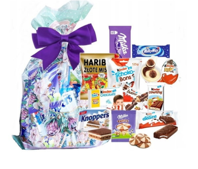 Słodki upominek: przezroczysty worek z kwiatowym motywem, zawiązany fioletową kokardą, wypełniony różnorodnymi słodyczami, w tym batonami Milka, Kinder, żelkami Haribo i waflami Knoppers na białym...