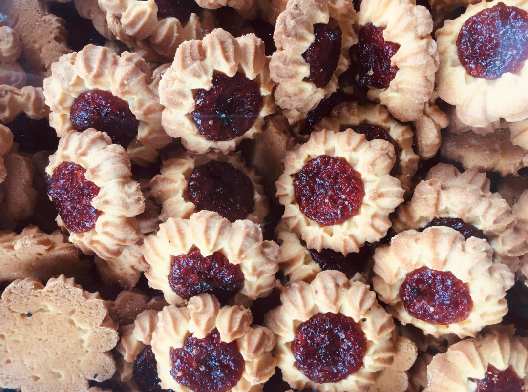 Kruche ciasteczka w kształcie kwiatów z marmoladą w środku, ułożone blisko siebie, widoczne drobne nierówności w teksturze ciasta.