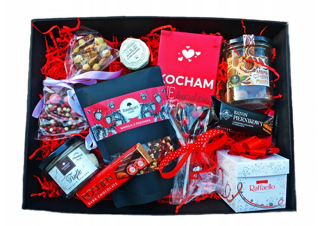 Czarny, otwarty karton wypełniony różnorodnymi słodyczami, orzechami, kawą i herbatą, zapakowanymi w ozdobne opakowania i przewiązane wstążkami. Widoczna jest książka z napisem 'Kocham Cię...