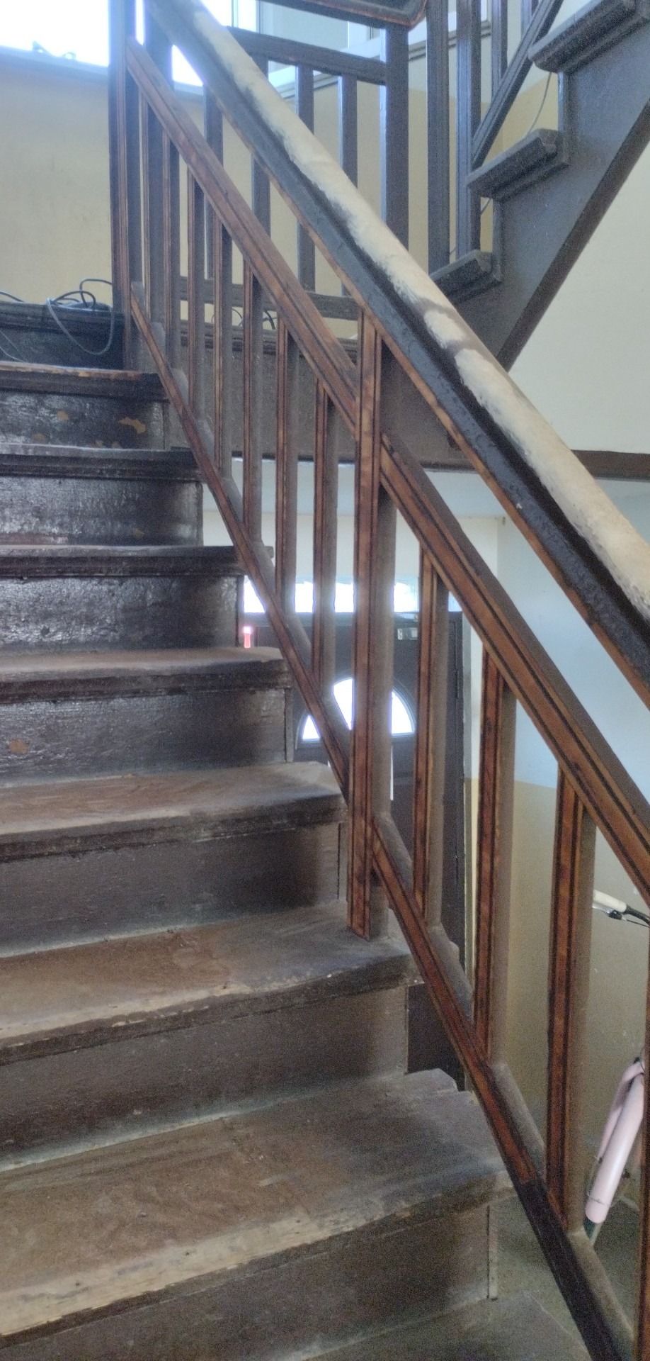 Drewniane schody z balustradą w trakcie renowacji, widoczne ślady farby i niedoskonałości na stopniach.