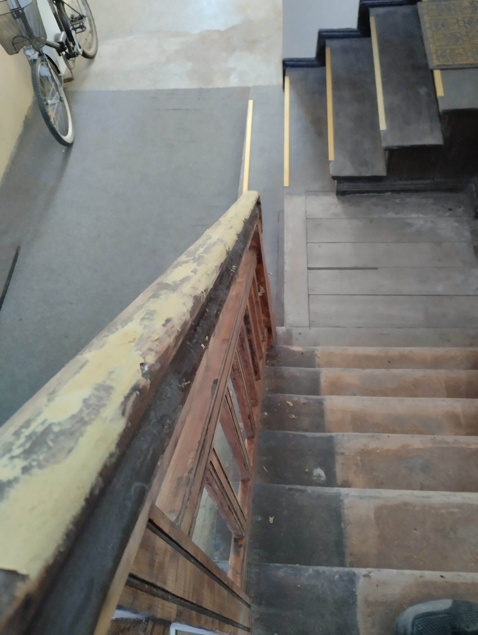 Klatka schodowa w Szczecinie przed remontem, widok z góry na drewnianą balustradę z łuszczącą się farbą i betonowe schody z widocznymi śladami użytkowania.
