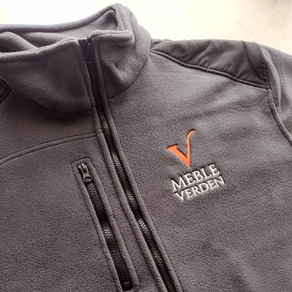 Szara bluza polarowa z zamkiem błyskawicznym i wyhaftowanym logo 'Meble Verden' w Siedlcach, widoczne detale zamków i przeszycia na ramionach.