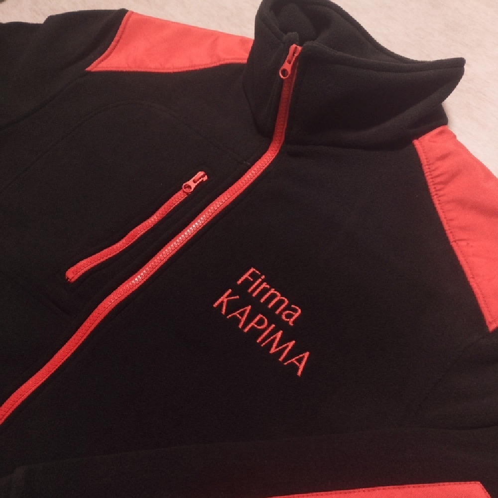 Czarno-czerwona bluza polarowa z wyhaftowanym logo firmy 'KAPIMA' w kolorze czerwonym, widoczne zamki błyskawiczne.