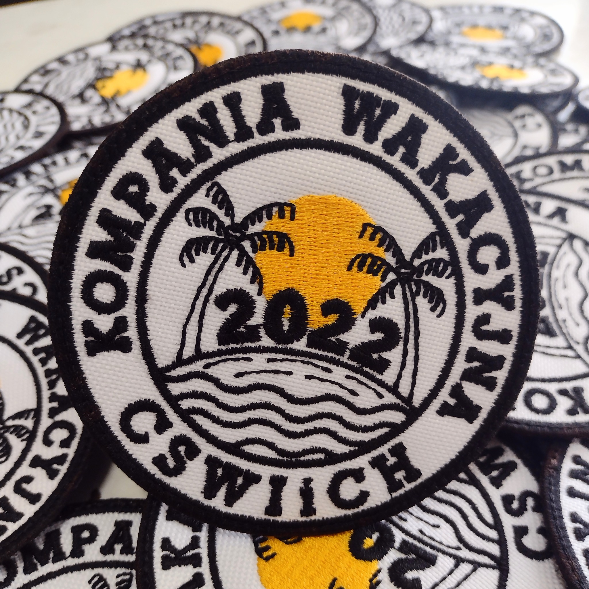 Okrągłe naszywki z wyhaftowanym motywem wakacyjnym: palmy, słońce, fale i napis 'Kompania Wakacyjna CS Wiich 2022'.