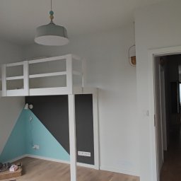 Paul & Zbig Usługi Remontowo - Budowlane Paweł Fijałkowski & Zbigniew Zalewski S.C. - Pokój dziecięcy z łóżkiem na antresoli, ściany pomalowane w geometryczne wzory: trójkąt turkusowy i prostokąt grafitowy, drewniana podłoga, widok na balkon i budynki za oknem.
