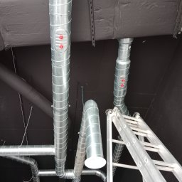 Vent klim - Montaż spiralnych kanałów wentylacyjnych z rewizjami i anemostatem na czarnym suficie, widoczna drabina aluminiowa.