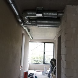 Vent klim - Wnętrze w trakcie montażu instalacji wentylacyjnej z widocznymi przewodami wentylacyjnymi pod sufitem, surowymi ścianami i narzędziami na podłodze.