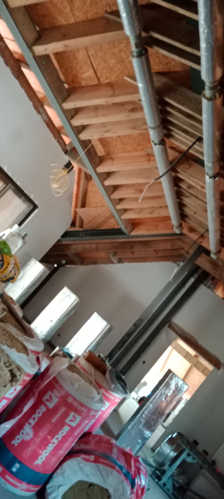 Poddasze w trakcie remontu z widoczną konstrukcją drewnianą dachu, izolacją Rockwool i instalacją wentylacyjną z rurami owiniętymi folią.