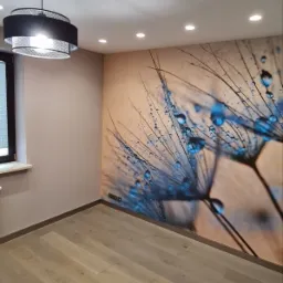 Pokój po remoncie z panelami podłogowymi w odcieniach szarości, ścianami w kolorze beżowym i fototapetą z motywem dmuchawca z kroplami wody, oświetlony lampą sufitową i halogenami.