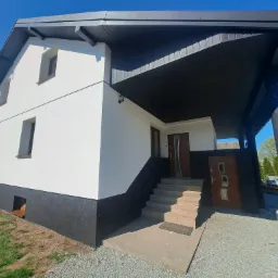 Biały dom z czarnym podbiciem dachu i cokołem, widok z zewnątrz, schody wejściowe, błękitne niebo, kontrastowe kolory.