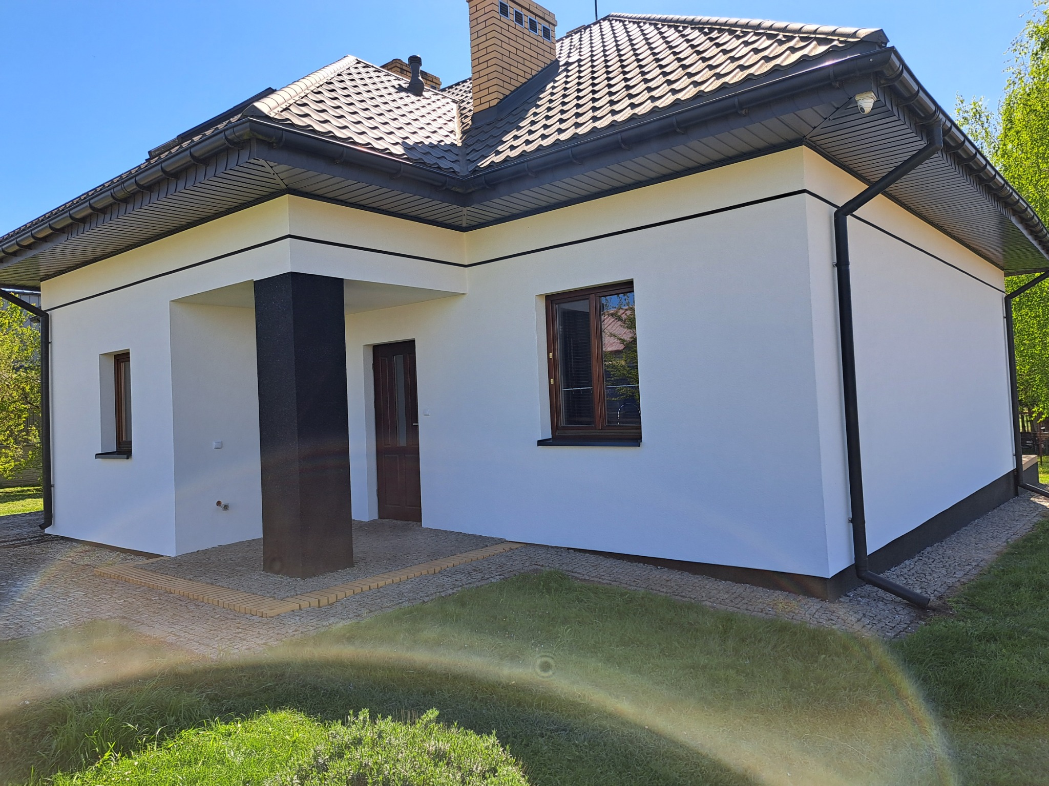 Biały dom jednorodzinny z brązowym dachem i ciemnymi detalami wykończeniowymi, widok z zewnątrz w słoneczny dzień. Nowoczesna elegancja.