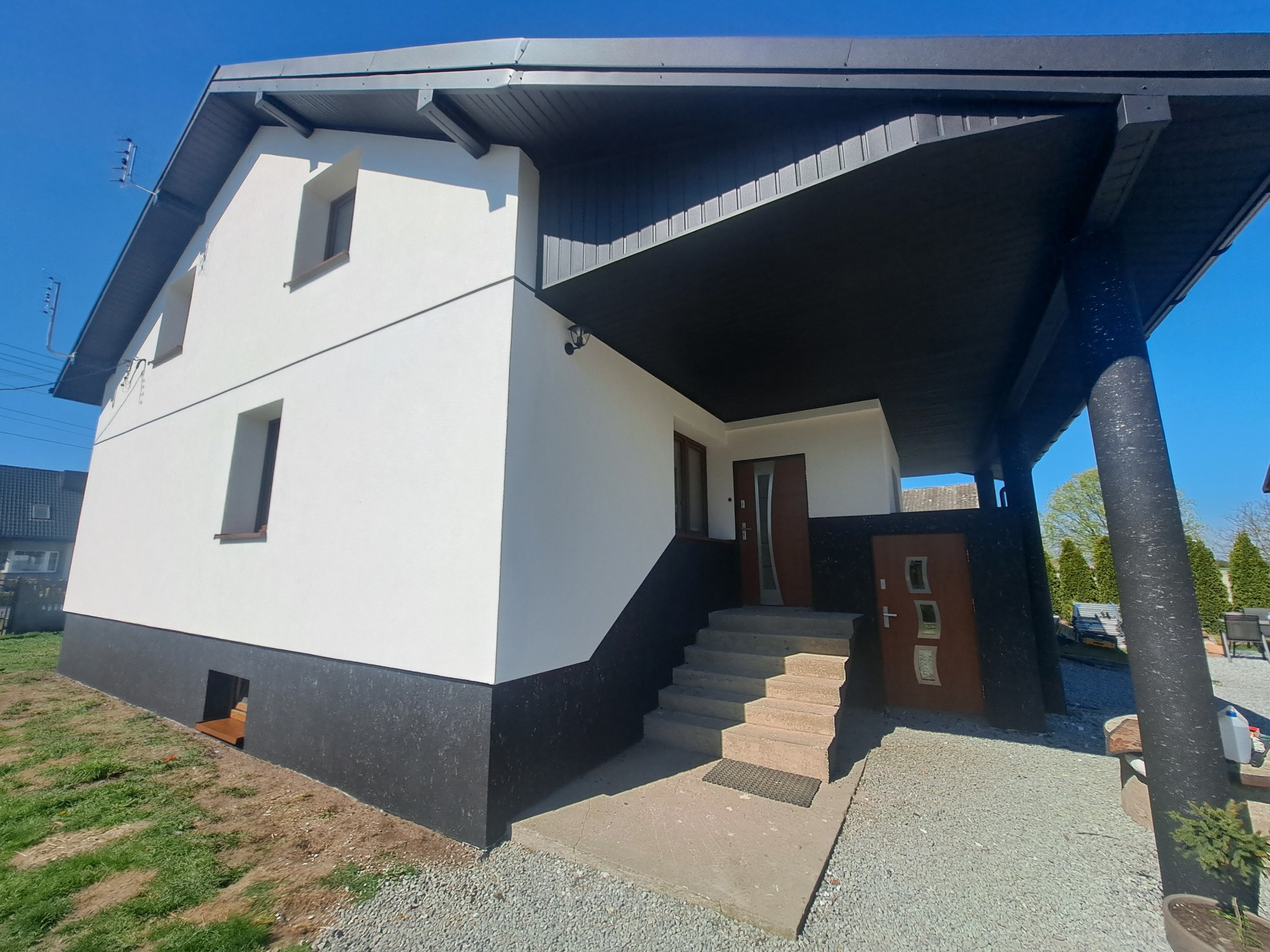 Biały dom z czarnym podbiciem dachu i cokołem, widok z zewnątrz, schody wejściowe, błękitne niebo, kontrastowe kolory.