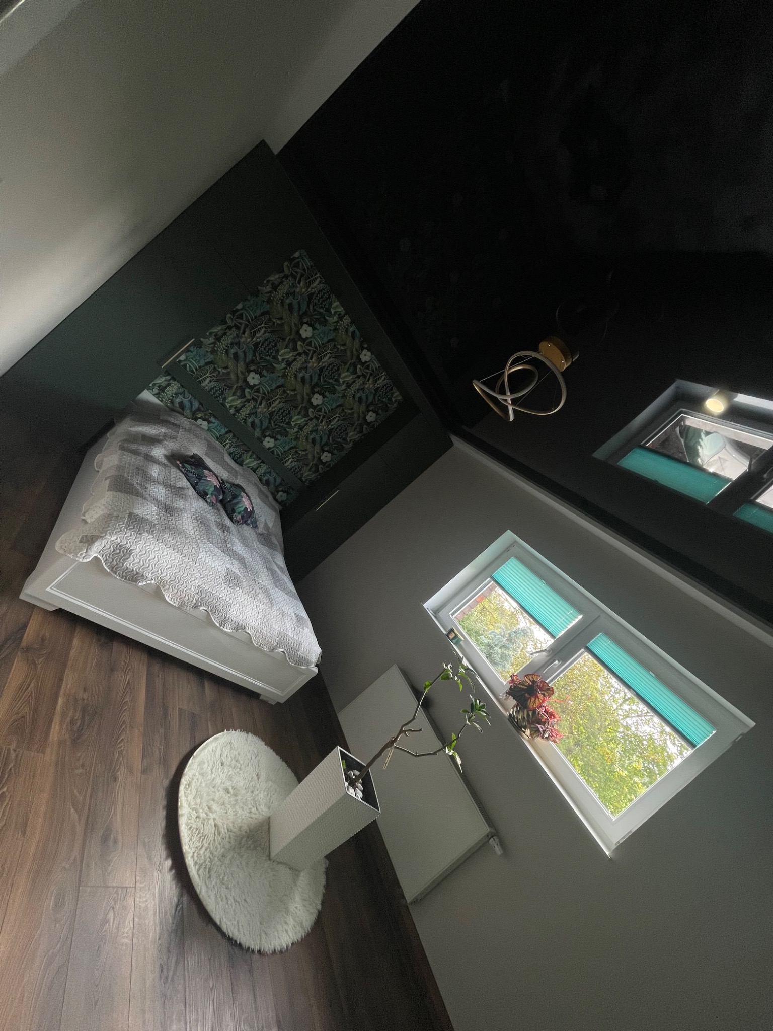 Sypialnia z czarnym sufitem, wzorzystą tapetą nad łóżkiem, białym łóżkiem i puszystym dywanem na drewnianej podłodze, widziana z góry pod kątem.