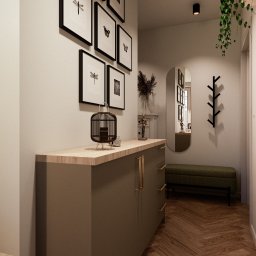PoKa Design - Nowoczesny przedpokój z komodą w kolorze khaki, dekoracjami i lustrem w owalnej ramie. Na ścianie grafiki w czarnych ramkach i wieszak na ubrania.