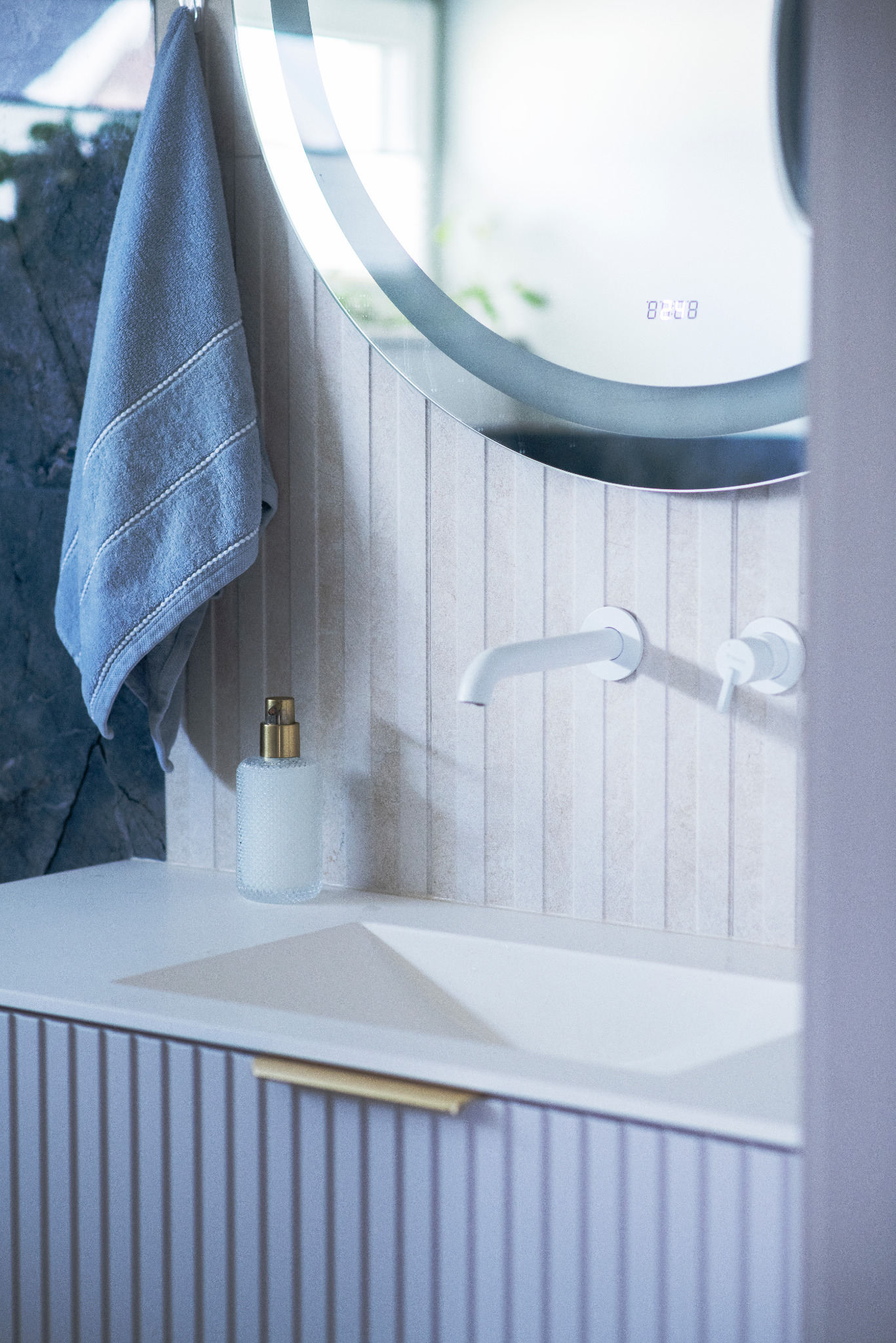 Nowoczesna łazienka z okrągłym lustrem z podświetleniem LED, białą umywalką wpuszczaną w szafkę z frezowanymi frontami i minimalistyczną armaturą.