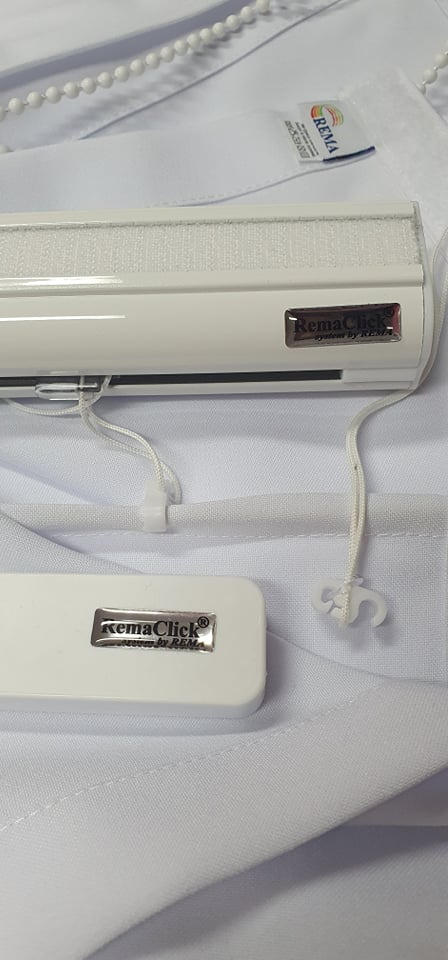 Detale mechanizmu sterującego białej rolety z widocznym logo producenta na tle białej tkaniny.