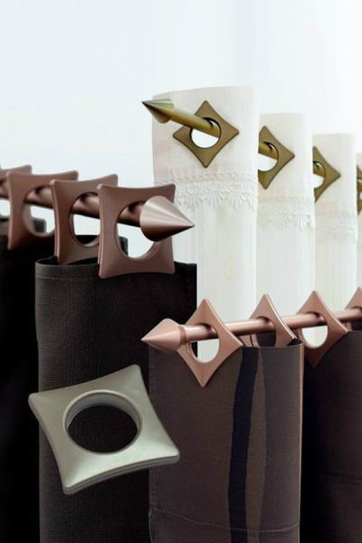 Dekoracyjne karnisze w kolorze miedzi z geometrycznymi zakończeniami i ozdobnymi przelotkami na zasłonach w odcieniach bieli i brązu.