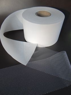 Rolka białej, półprzezroczystej tkaniny na czarnym tle, z widoczną siatkową strukturą materiału.